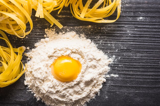 Gema de ovo com farinha e tagliatelle cru no contexto de madeira