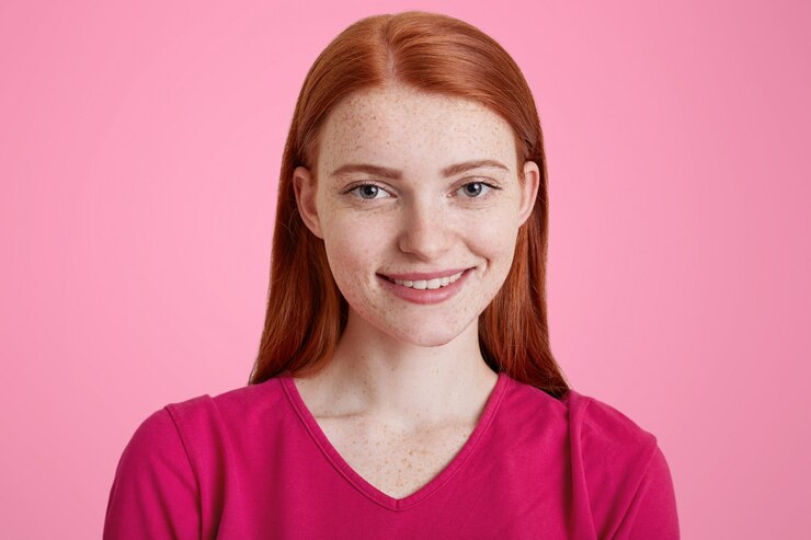 Foto grátis gengibre feminino com sorriso agradável, tem pele sardenta, sendo feliz por ser fotografado, vestido de camisola rosa