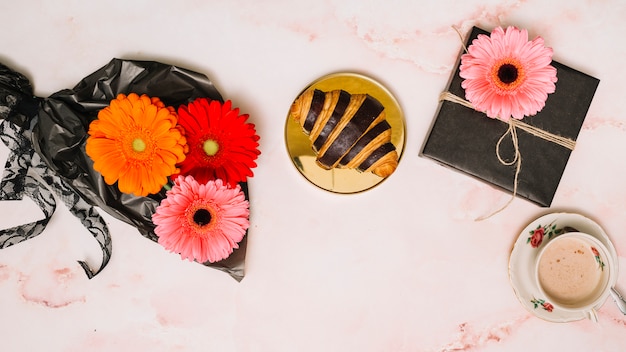 Foto grátis gerbera flores na embalagem de filme com caixa de presente e croissant