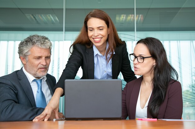 Gerente confiante e alegre, compartilhando ideias com colegas, mostrando a apresentação no computador.