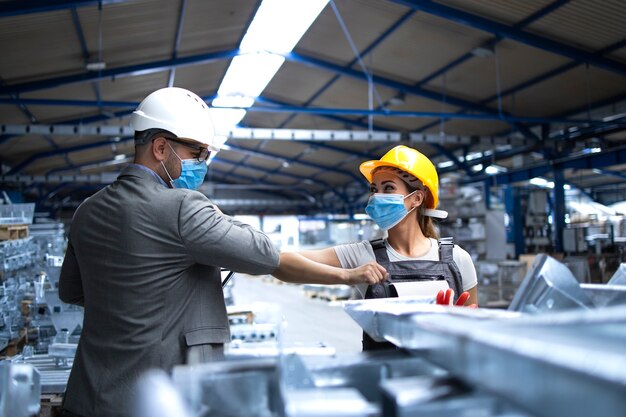 Gerente da fábrica visitando a linha de produção e cumprimentando o trabalhador com cotovelos devido ao vírus corona