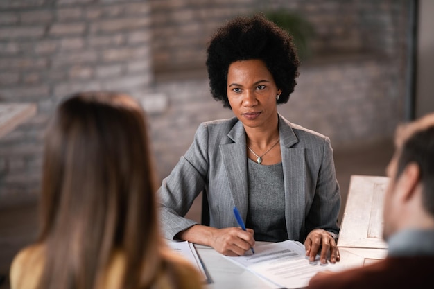 Gerente de banco afro-americano tendo uma entrevista com seus clientes e arquivando a papelada durante a reunião