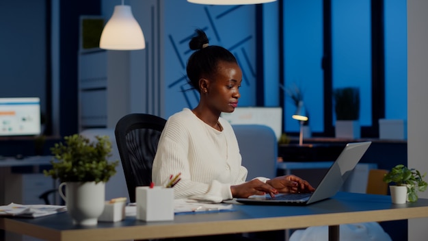 Foto grátis gerente ocupado trabalhando em relatórios financeiros, verificando gráficos de estatísticas, digitando no laptop sentado à mesa tarde da noite no escritório inicial, fazendo horas extras para respeitar o prazo do projeto financeiro