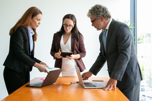 Gerente sênior de óculos discutindo com mulheres de negócios e usando laptop