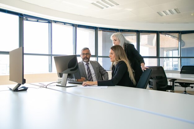 Gerentes da empresa discutindo a solução. Empresários se reunindo na sala de reuniões, assistindo conteúdo no monitor do computador juntos. Comunicação empresarial ou conceito de trabalho em equipe