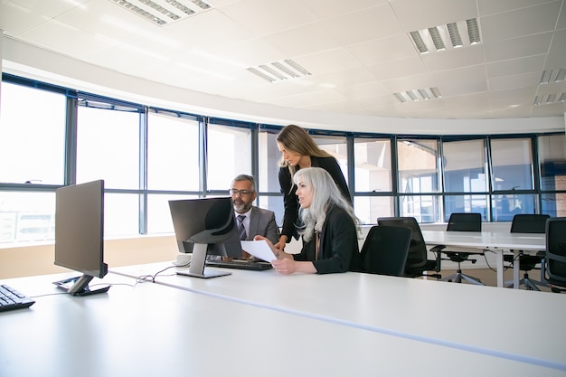 Gerentes da empresa reunidos na sala de reuniões, assistindo à apresentação do projeto no monitor do computador juntos, segurando um relatório em papel. comunicação empresarial ou conceito de trabalho em equipe