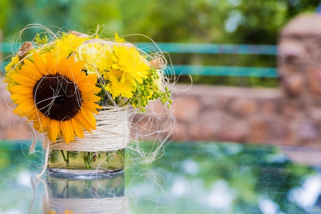 Girassol e flores amarelas em um pequeno vaso colocado ao ar livre sobre uma mesa