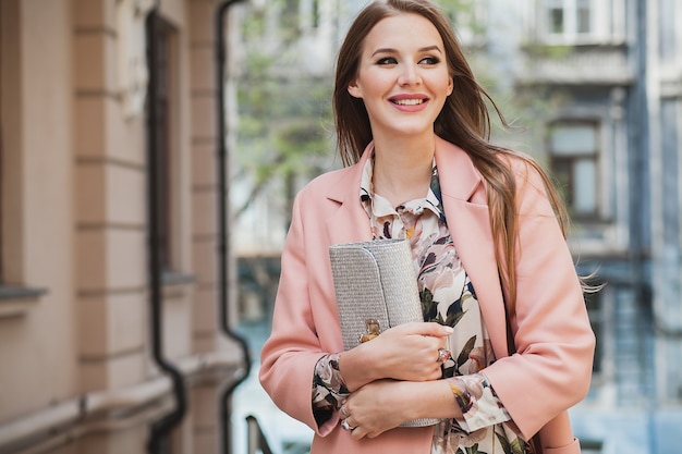 Glam atraente elegante sorridente mulher caminhando pelas ruas da cidade com casaco rosa tendência da moda de primavera segurando bolsa