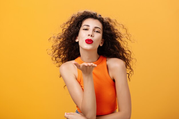 Glamour, mulher elegante, confiante e sensual, com penteado encaracolado e batom vermelho, dobrando os lábios segurando ...