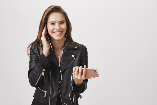 Glamour sorridente mulher desfrutando de ouvir música em fones de ouvido, segure smartphone