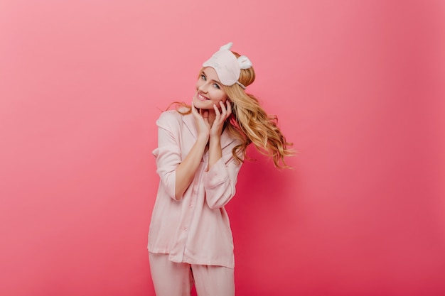Glamourosa garota encaracolada expressando energia pela manhã. agradável mulher caucasiana em pijama de seda, posando na parede rosa.