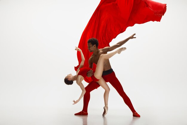 Graciosos dançarinos de balé clássico dançando isolado no fundo branco do estúdio. Casal com roupas vermelhas brilhantes como uma combinação de vinho e leite. O conceito de graça, artista, movimento, ação e movimento.
