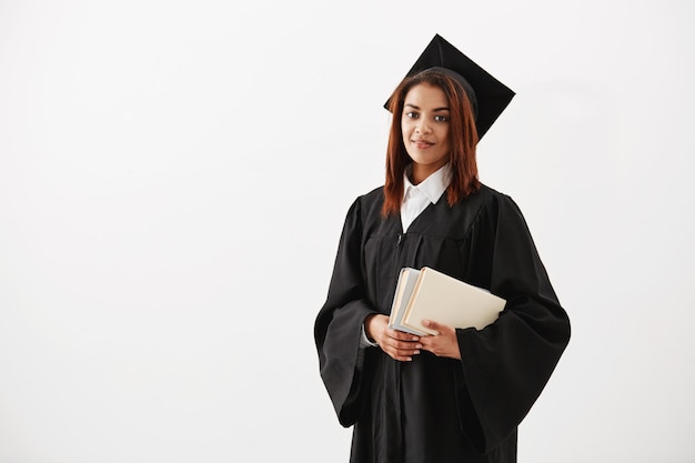 Graduado africano feminino alegre bonito sorrindo segurando livros. Copie o espaço.