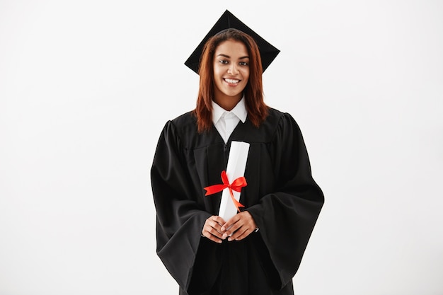 Graduado fêmea africano que sorri guardando o diploma.
