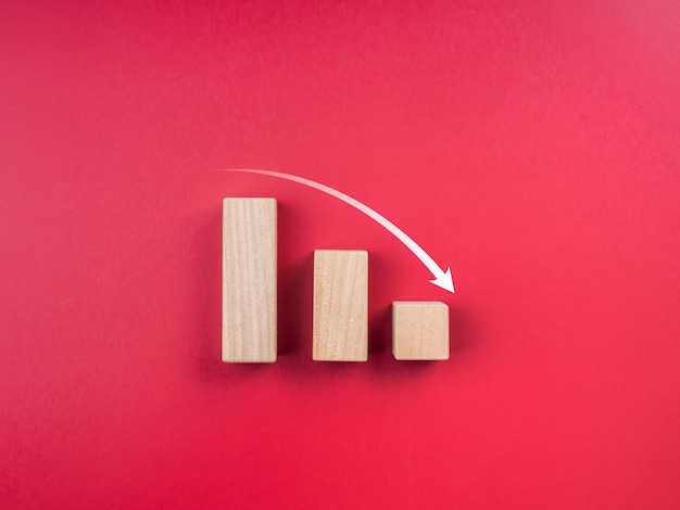 Gráfico com tendência de queda. conceito de crise empresarial. seta para baixo em três etapas do gráfico de blocos de madeira sobre fundo vermelho, com espaço de cópia, estilo minimalista.