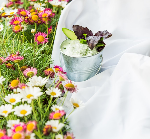 Grama com flores, toalha de mesa de piquenique e um copo de iogurte com ervas.