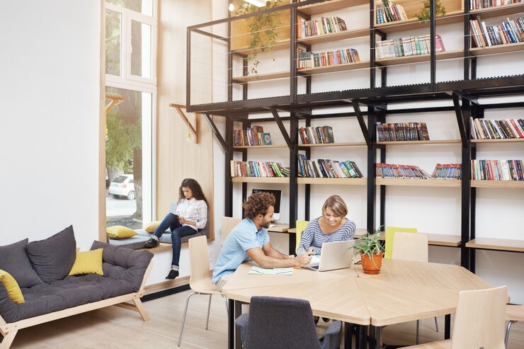 Foto grátis grande biblioteca moderna de manhã. duas pessoas sentadas, olhando no monitor do laptop falando sobre o projeto de inicialização. menina sentada no peitoril da janela, lendo o livro no smartphone, passar um tempo antes do estudo.