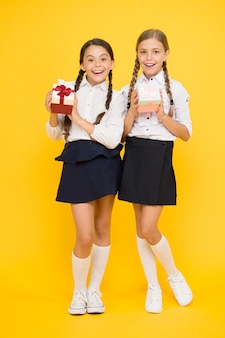 Grande dia de compras. meninas felizes comprando presentes à venda em fundo amarelo. crianças sorridentes com papel colorido apresentam caixas com uniforme escolar. conceito de compras de férias.