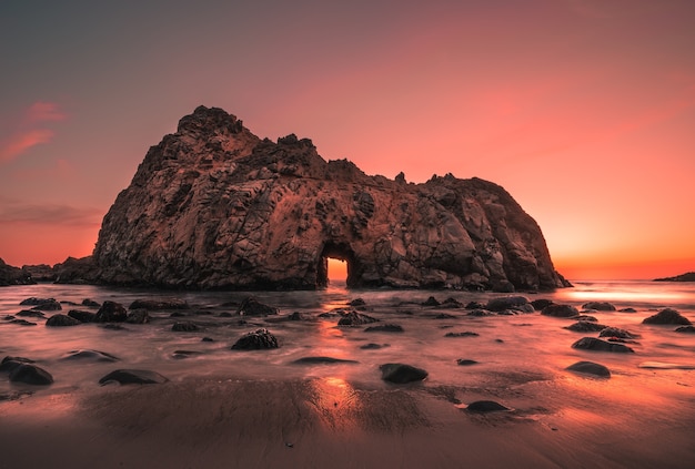 Grande penhasco na Praia Pfeiffer, nos EUA, durante o pôr do sol