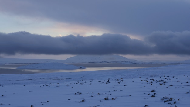Grande plano de uma costa de neve perto de água congelada sob um céu nublado