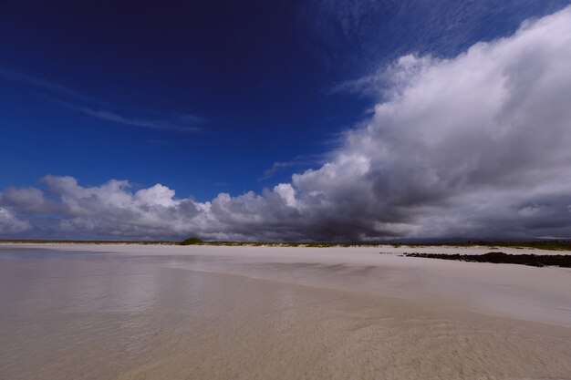 Grande plano de uma costa do mar com um campo gramado à distância e nuvens em um céu azul escuro