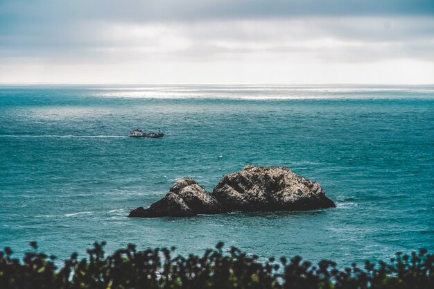 Grandes rochas no meio do mar e uma guarda costeira navegando à distância