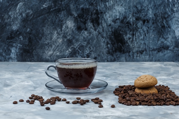 Grãos de café de close-up com uma xícara de café, cookies em fundo de mármore azul escuro e azul claro. horizontal