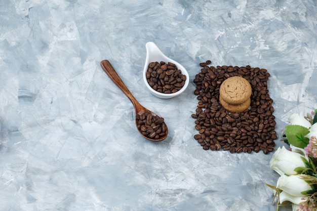 Foto grátis grãos de café de close-up na colher de pau, jarro de porcelana branca com biscoitos, flores sobre fundo de mármore azul claro. horizontal