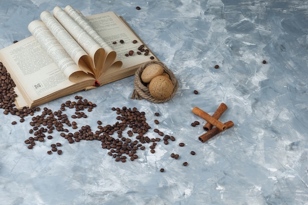 Grãos de café de vista de alto ângulo com livro, canela, biscoitos, cordas sobre fundo de mármore azul claro. horizontal