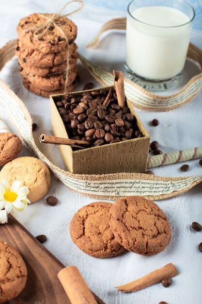 Grãos de café e biscoitos de manteiga com um copo de leite numa toalha de mesa azul