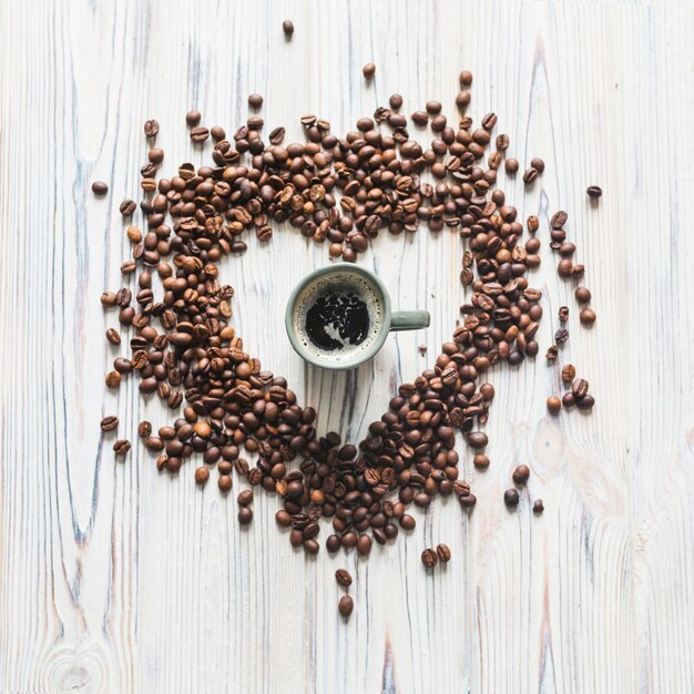 Grãos de café em forma de coração em torno do copo de café