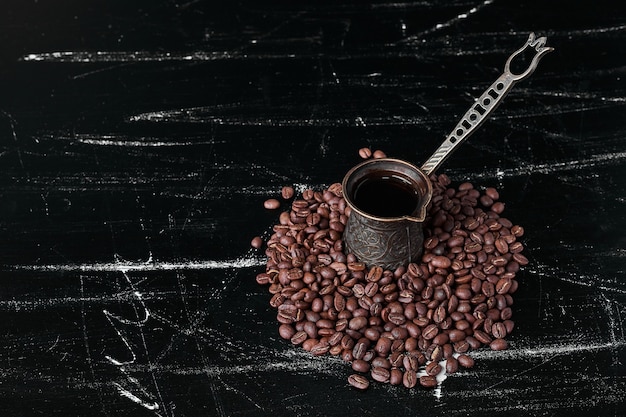 Grãos de café em fundo preto com uma panela metálica.