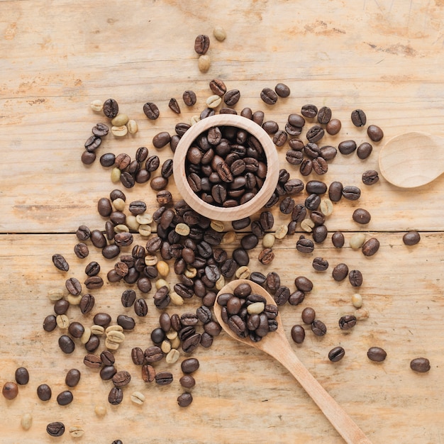 Grãos de café em recipiente de madeira e na mesa com colher