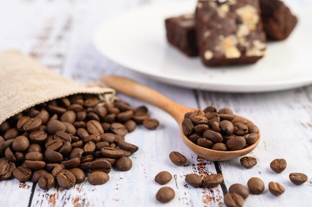 Grãos de café em sacos de colher e cânhamo de madeira em uma mesa de madeira branca.