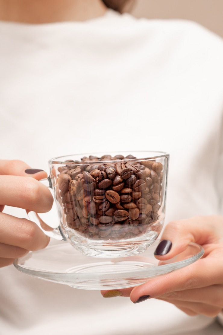 Foto grátis grãos de café em um copo de vidro nas mãos femininas.