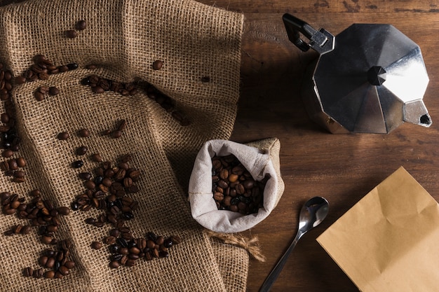 Grãos de café espalhados em pano de saco perto de saco, cafeteira e pacote