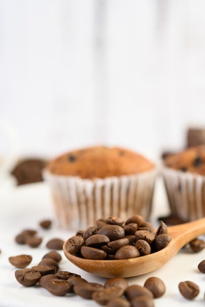 Grãos de café na colher de pau e cupcakes de banana em uma mesa de madeira branca.