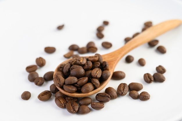 Grãos de café na colher de pau em uma mesa de madeira branca.