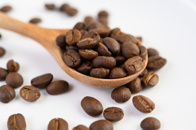 Grãos de café na colher de pau em uma mesa de madeira branca.