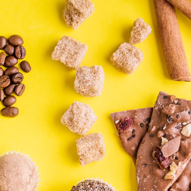 Grãos de café; trufas; cubos de açúcar mascavo e barra de chocolate de frutas secas em pano de fundo amarelo