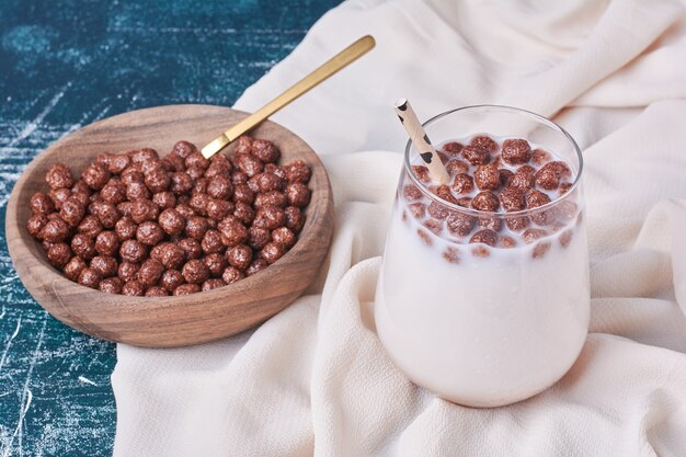 Grãos de chocolate com uma xícara de leite em azul.