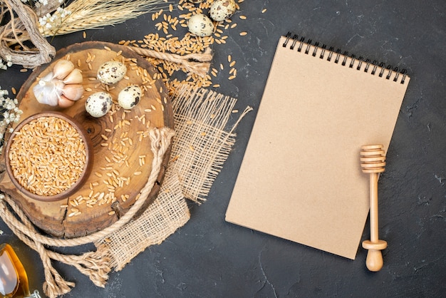 Grãos de trigo de vista superior em uma tigela de alho na placa de madeira natural ovos de codorna caderno mel na mesa