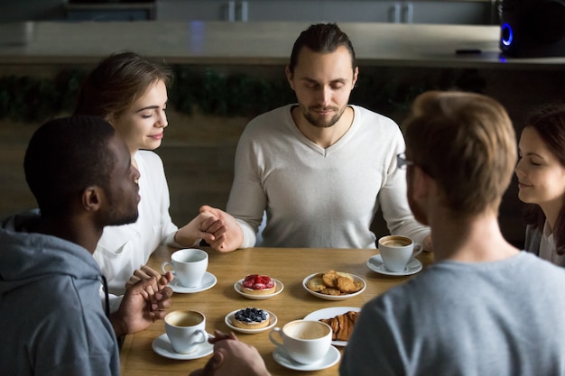 Foto grátis grato amigos multirraciais sentados juntos na mesa de café dizendo graça