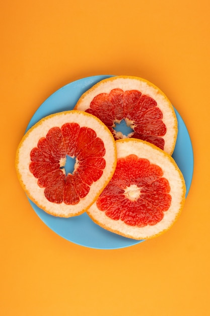 Foto grátis greapefruit, uma vista superior de três pedaços de frutas dentro da placa azul na mesa laranja