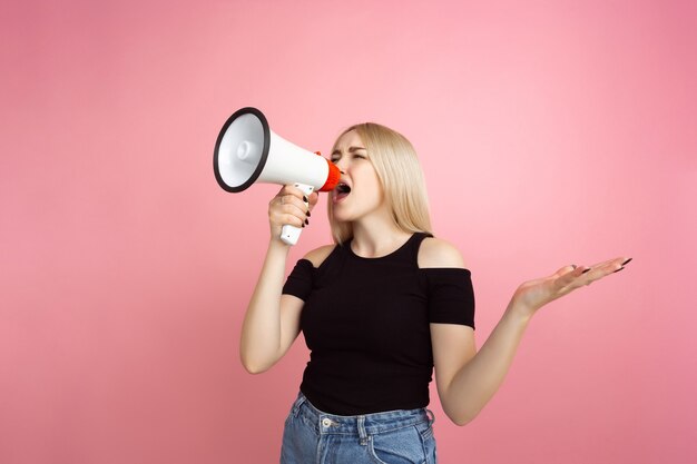 Gritando com megafone. Retrato de jovem com emoções brilhantes na parede do estúdio rosa coral