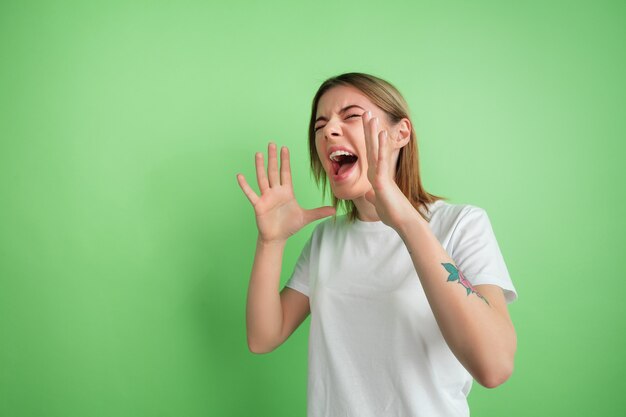 Gritando, gritando. Retrato de mulher jovem branca isolado na parede verde do estúdio