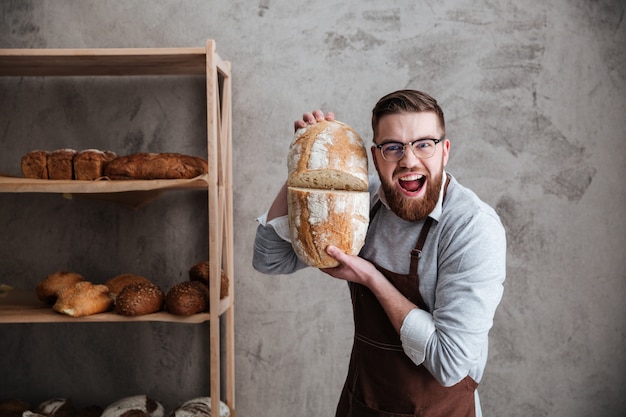 Foto grátis gritando jovem padeiro de pé na padaria segurando o pão