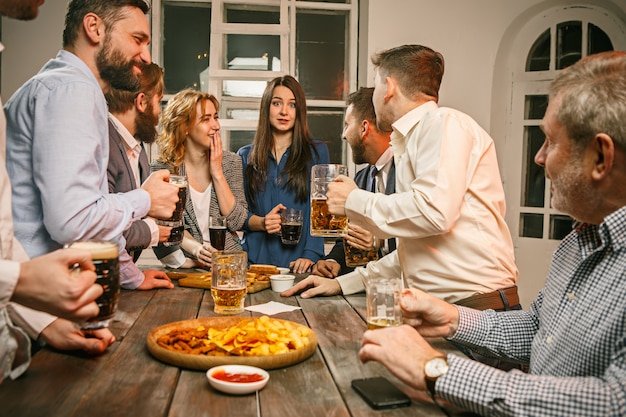 Grupo de amigos apreciando bebidas à noite com cerveja na mesa de madeira