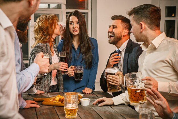 Grupo de amigos apreciando bebidas à noite com cerveja na mesa de madeira