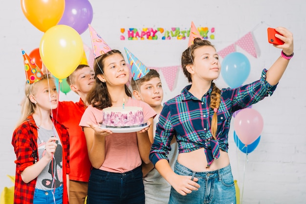 Grupo de amigos com bolo de aniversário tomando selfie no celular